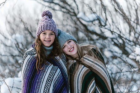 girl and woman wearing knit caps and assorted-color blankets near bare trees covered with snow during daytime thumbnail