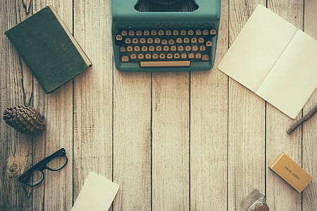 teal and white typewriter beside white printer paper on the top of brown wooden board thumbnail