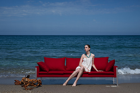 woman sitting on red futon on shoreline under blue and white sky thumbnail