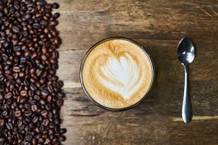 clear cup filled with cappuccino beside spoon on brown surface thumbnail