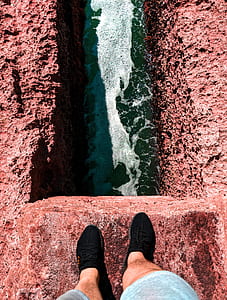 person standing on cliff above body of water thumbnail