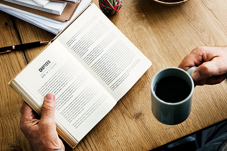 person holding mug and opened book thumbnail