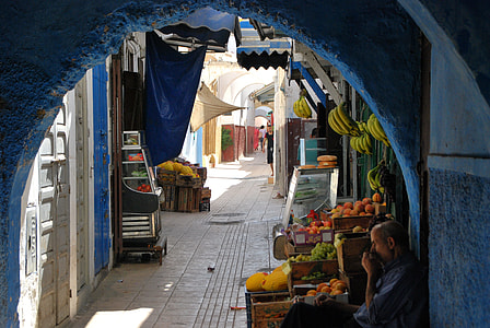 man leaning on wall beside his fruit stand in an alley thumbnail