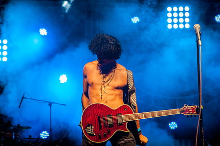man carrying red whiskered guitar standing on lighted stage thumbnail