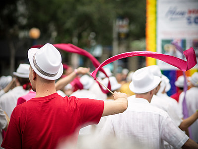 man in red crew-neck T-shirt and white hat holding stick with red lace thumbnail