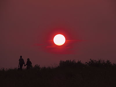 silhouette photography of two person walking on grass field during full moon thumbnail