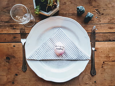 white egg on white ceramic plate between fork and bread knife on brown wooden panel thumbnail
