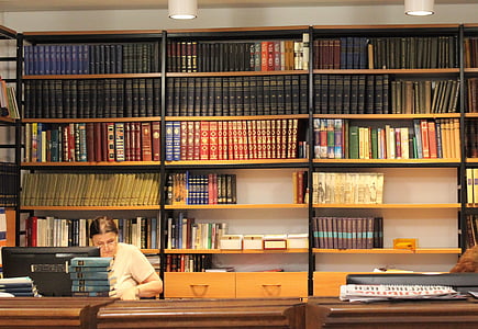woman wearing white shirt sitting on chair facing flat screen computer monitor in library thumbnail
