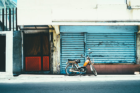 orange and black moped parked near closed storefront thumbnail