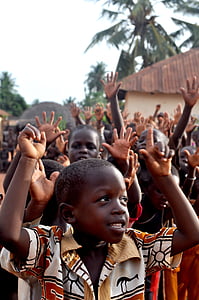 group of children raising hands near trees and building during daytime thumbnail