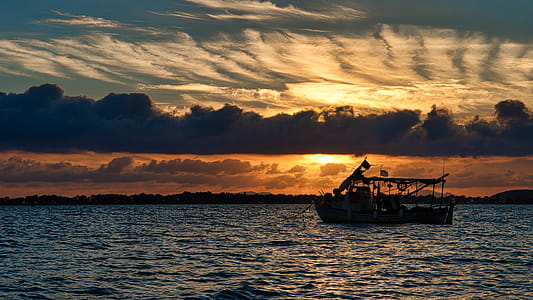 Silhouette Photo of Boat on Ocean during Golden Hour thumbnail