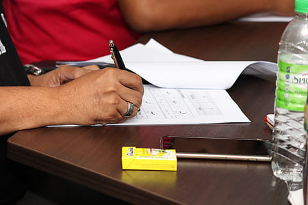 person holding ballpoint pen over white printer paper thumbnail