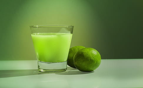 glass of lime juice beside two limes thumbnail