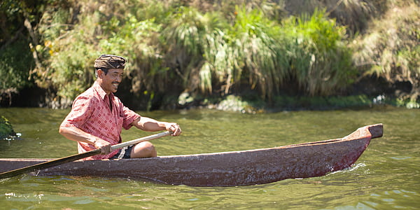 man in pink collared top riding boat on body of water thumbnail