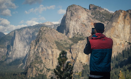 man holding black smartphone while taking a photo of brown mountains under cloudy sky during daytime thumbnail
