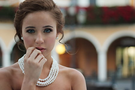 selective photo of woman with right hand on lips wearing pearl necklace thumbnail