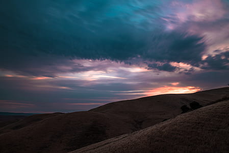 brown mountains under cloudy sky during sunset thumbnail