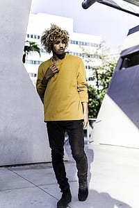 man wearing yellow long-sleeved shirt and black jeans standing near wall thumbnail