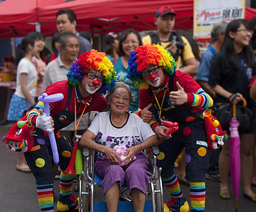 woman on wheelchair in between two clown in festivity during daytime thumbnail