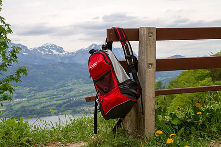 black, red, and gray backpack hanging on brown wooden fence thumbnail