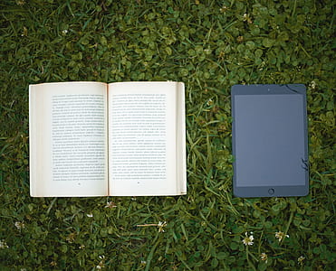 black iPad beside beige book on green grass thumbnail