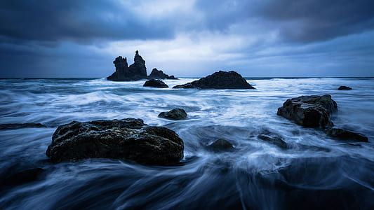 timelapse photo of body of water with black rocks under cloudy skies thumbnail