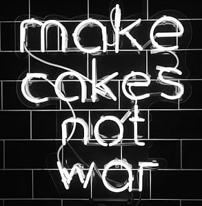 make cakes not war neon signage on black wall thumbnail