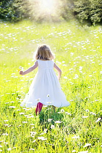 girl in white tank dress walking on green grass with white petaled flower field thumbnail