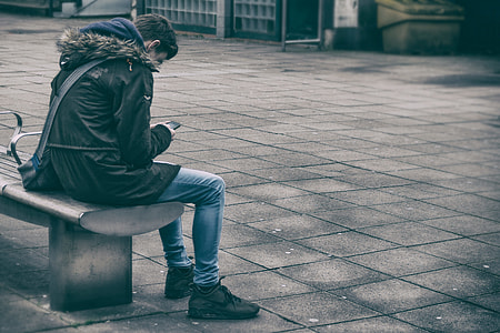 man in black jacket sitting on bench holding smartphone thumbnail