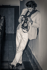 gray scale photography of man in gray suit jacket leaning on wall while holding DSLR camera thumbnail