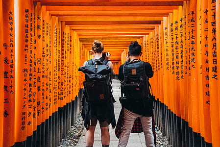 photography of woman and man taking photo near orange wooden arc during daytime thumbnail