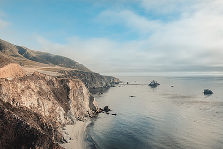 hill over body of water under white clouds and blue sky thumbnail