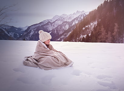 toddler girl in snowsuit and cable knit pom knit cap lying on snow ground thumbnail