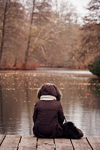 person in black coat sitting on wood above body of water thumbnail