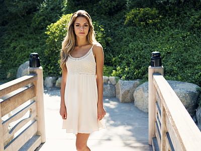 smiling woman wearing white spaghetti strap dress in between wooden railings during daytime thumbnail