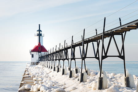 Red and White Concrete Lighthouse Surrounded by Snow Near Body of Water thumbnail