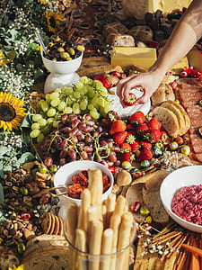 person picking red strawberry on table with assorted fruits and pastries thumbnail