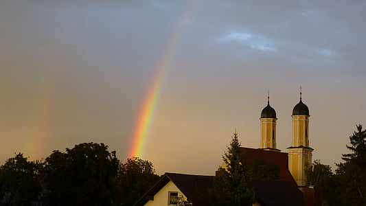 white building with two towers near trees under white clouds and rainbow during daytime thumbnail