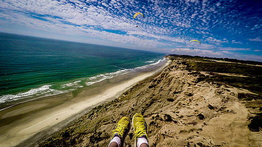 person wearing pair of black-and-yellow lace-up shoes near body of water under blue and white sky at daytime thumbnail