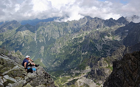 man sitting on gray rock viewing green and gray rocky mountains during daytime thumbnail