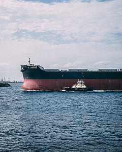 black boat near cargo ship on body of water thumbnail