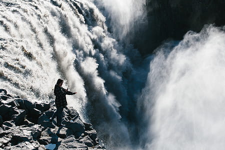 woman standing on grey rocks on top of waterfalls during daytime thumbnail