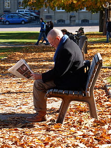 man sitting on bench while reading newspaper thumbnail