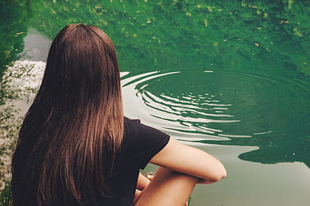 woman sitting on rock beside body of water thumbnail