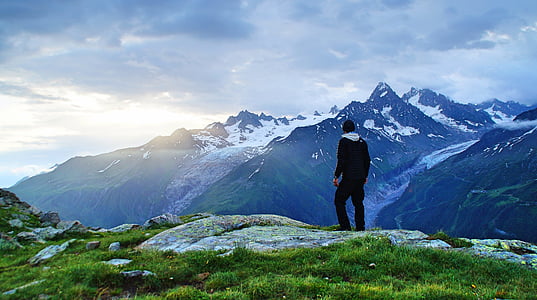 man standing on cliff fronting mountain covered with snow thumbnail