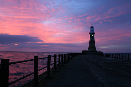 silhouette of lighthouse on wooden dock under pink and blue sky thumbnail