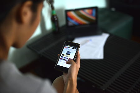 woman using phone beside laptop computer thumbnail