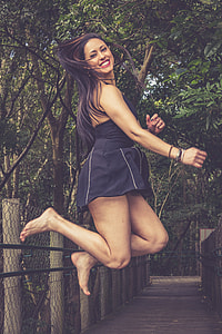 woman wearing black halter dress jumping under green trees thumbnail