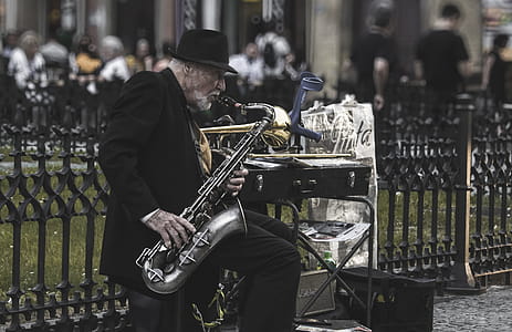 Man Sitting on Stool While Playing Saxophone Beside Fence thumbnail