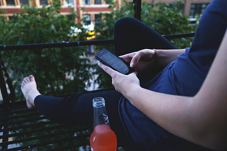 person holding black iPhone 5 sitting beside glass bottle thumbnail